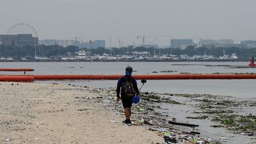File photo of a man filming while walking past garbage on a beach in Manila.