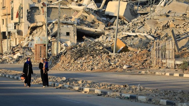 Displaced Palestinians walk past destroyed buildings in al-Bureij refugee camp in the central Gaza Strip