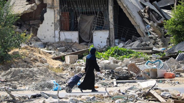 A Palestinian woman walks past destroyed buildings, Gaza