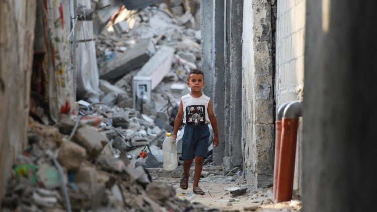 A Palestinian boy carries an empty container as he walks in a rubble-covered alley in Khan Yunis