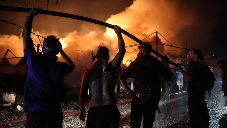 Voluntarios sostienen una manguera de agua para ayudar a los bomberos a extinguir un incendio en una fábrica de madera en Vrilissia, en las afueras de Atenas