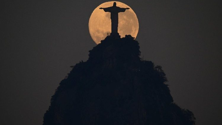 A lua cheia se põe atrás da estátua do Cristo Redentor no Rio de Janeiro, em 20 de agosto de 2024. (Foto de Pablo PORCIUNCULA / AFP)