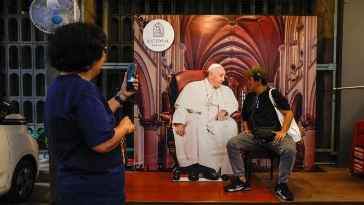 Um fiel católico posa para uma fotografia ao lado de uma imagem recortada do Papa Francisco antes de sua visita à Catedral de Jacarta, Indonésia, 28 de agosto de 2024.