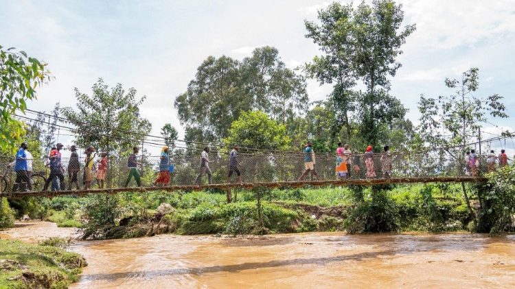 Residents walk over a water bridge after their homes were swamped following rains that triggered flooding and landslides in Rubavu district