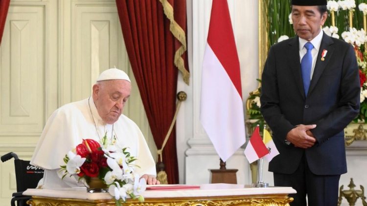 Pope Francis signs the Book of Honour with President Joko Widodo standing beside him