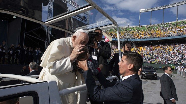 El Papa besa a un niño durante el saludo a los fieles, Loïc Rossier a su lado