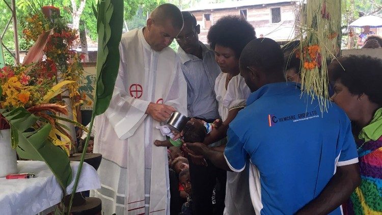 A missionary priest baptizes a baby in Papua New Guinea